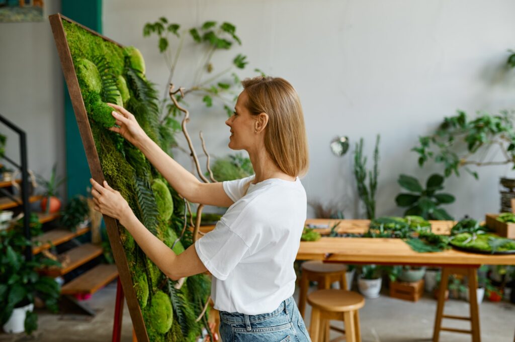 Young happy florist decorator creating plant moss panel